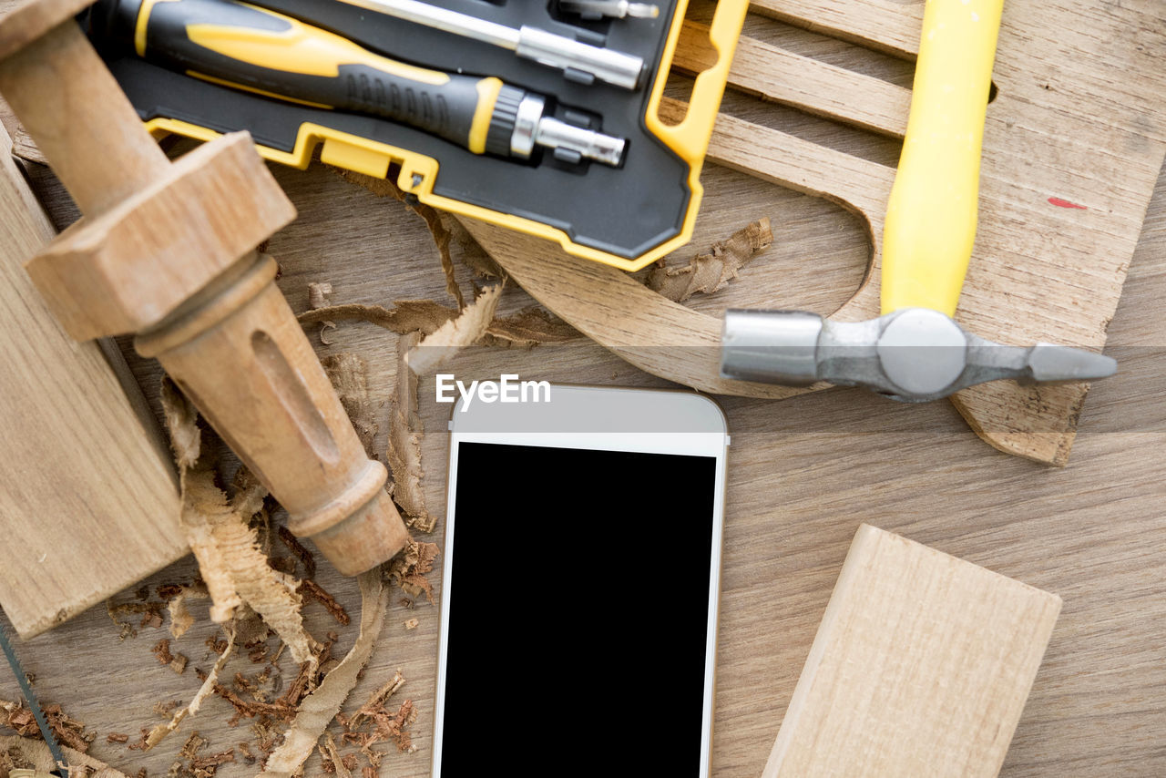 Directly above shot of mobile phone with wood and hand tools on table