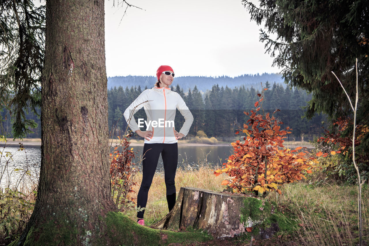 Full length of mature woman with arms akimbo standing against trees in forest