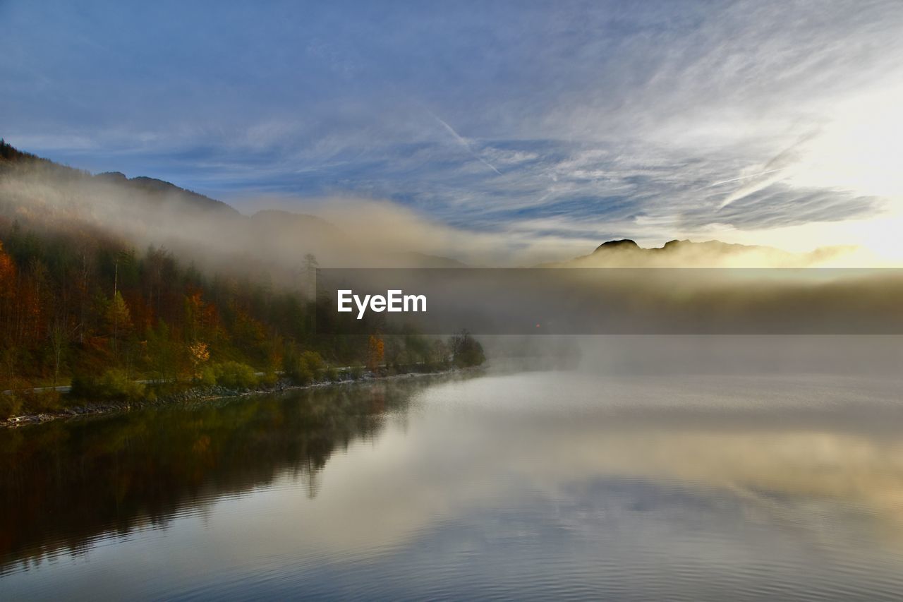 Scenic view of lake with fog against sky during sunset