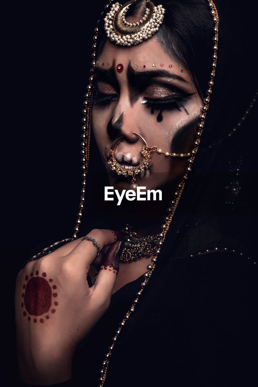 Close-up of young woman in traditional clothing with spooky make-up against black background