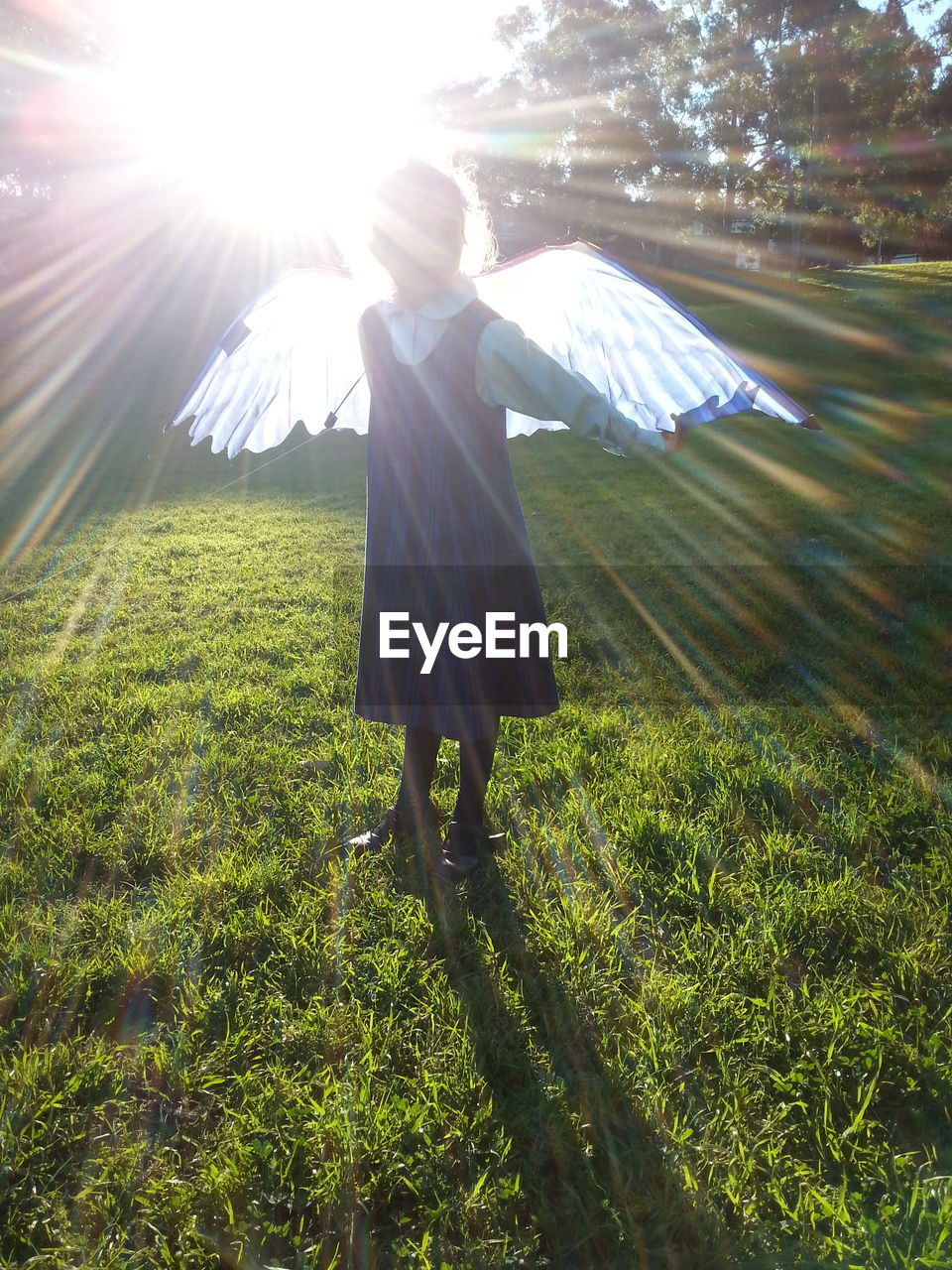 Girl wearing angel costume while standing on grassy field on sunny day