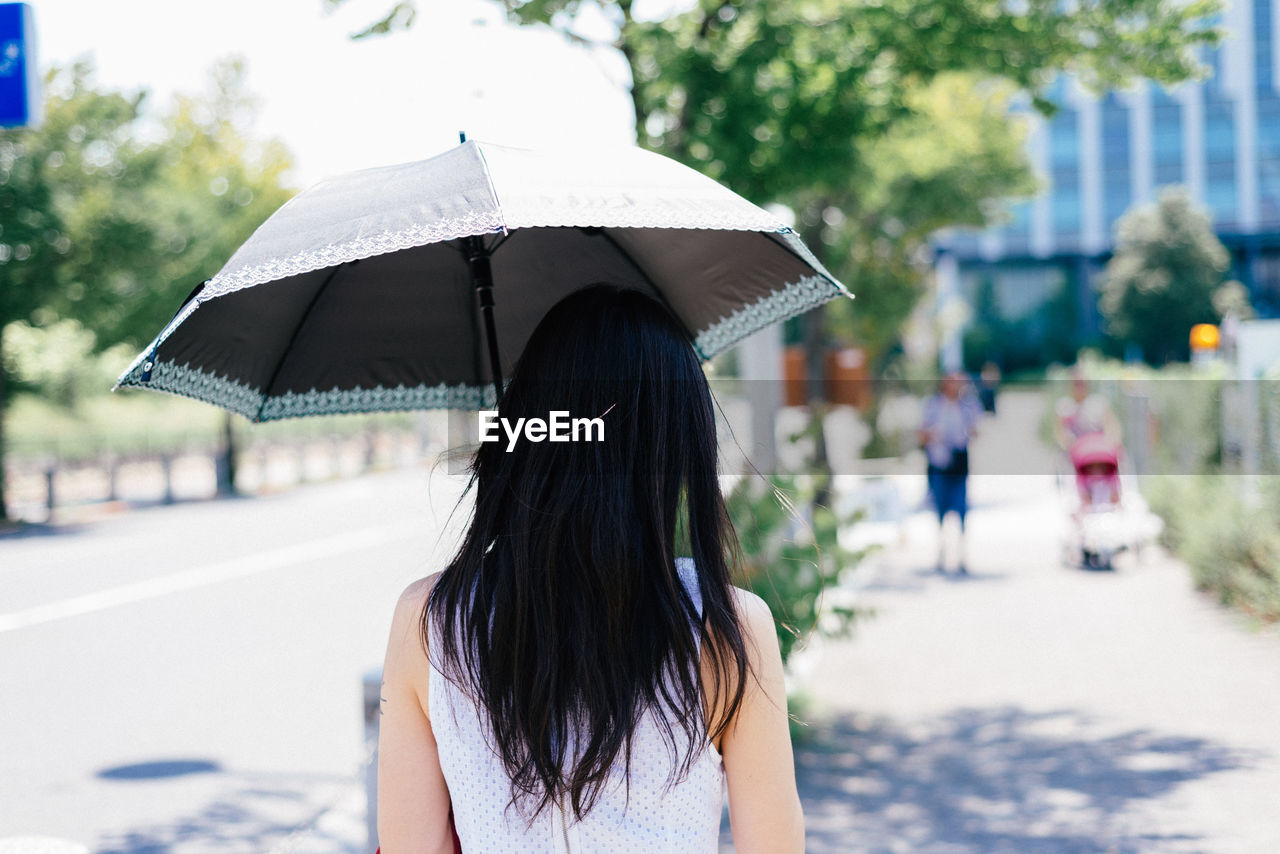 Rear view of woman walking under umbrella during sunny day in city