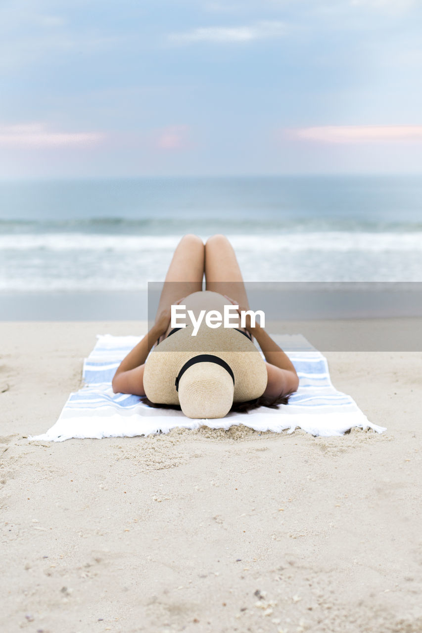 Pregnant woman wearing bikini and sunhat laying on beach