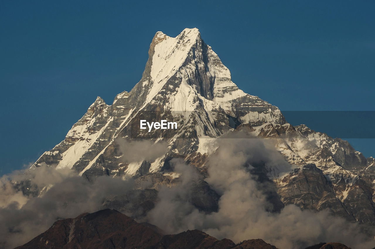 Low angle view of snowcapped mountain against clear blue sky