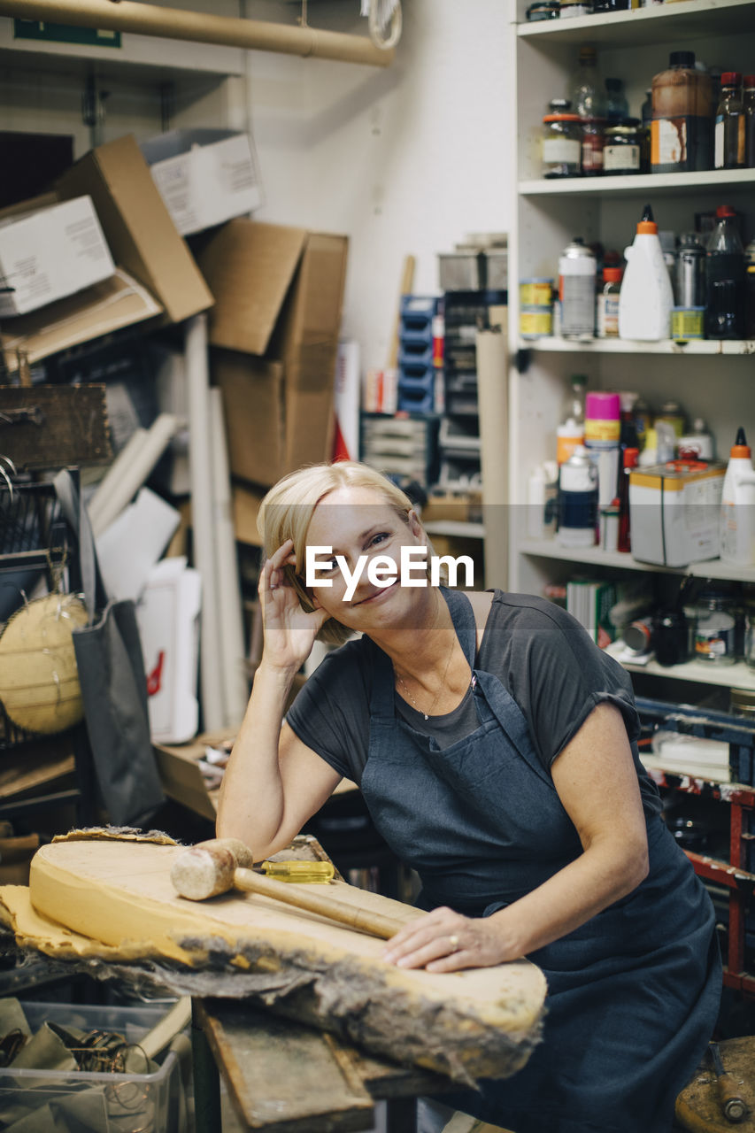 Portrait of confident female upholstery worker sitting at workbench in workshop