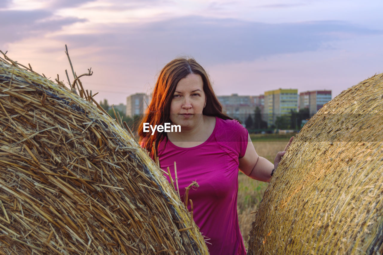 straw, hay, agriculture, one person, adult, bale, sky, landscape, women, nature, rural scene, portrait, plant, young adult, farm, smiling, long hair, crop, haystack, field, hairstyle, cloud, looking at camera, land, standing, harvesting, architecture, outdoors, casual clothing, lifestyles, brown hair, front view, environment, waist up, day, happiness, occupation, grass, cereal plant, three quarter length, leisure activity, rural area, sunlight