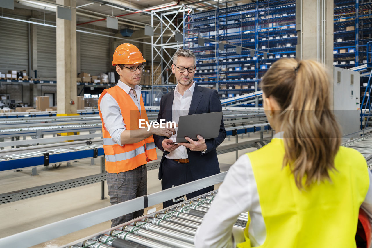 Mature manager discussing with colleague over laptop in factory