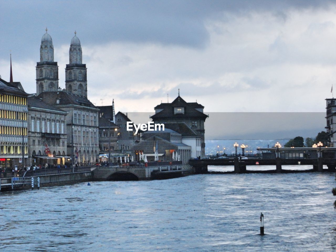 RIVER IN CITY AGAINST CLOUDY SKY