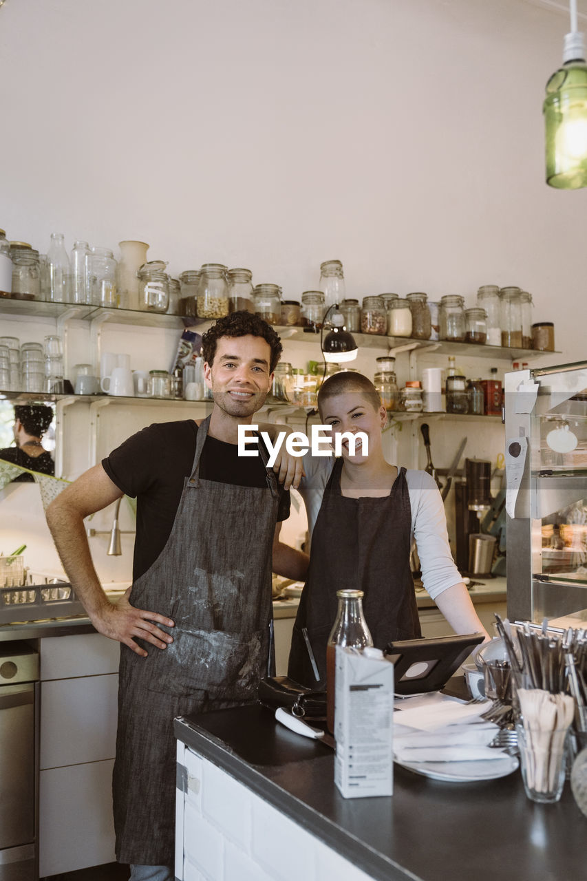 Portrait of happy male and female business owners standing together at cafe