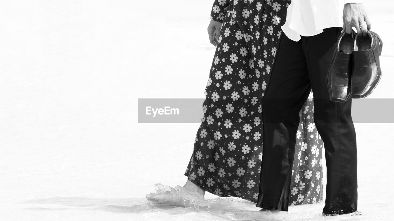 LOW SECTION OF WOMAN WITH UMBRELLA ON WHITE BACKGROUND