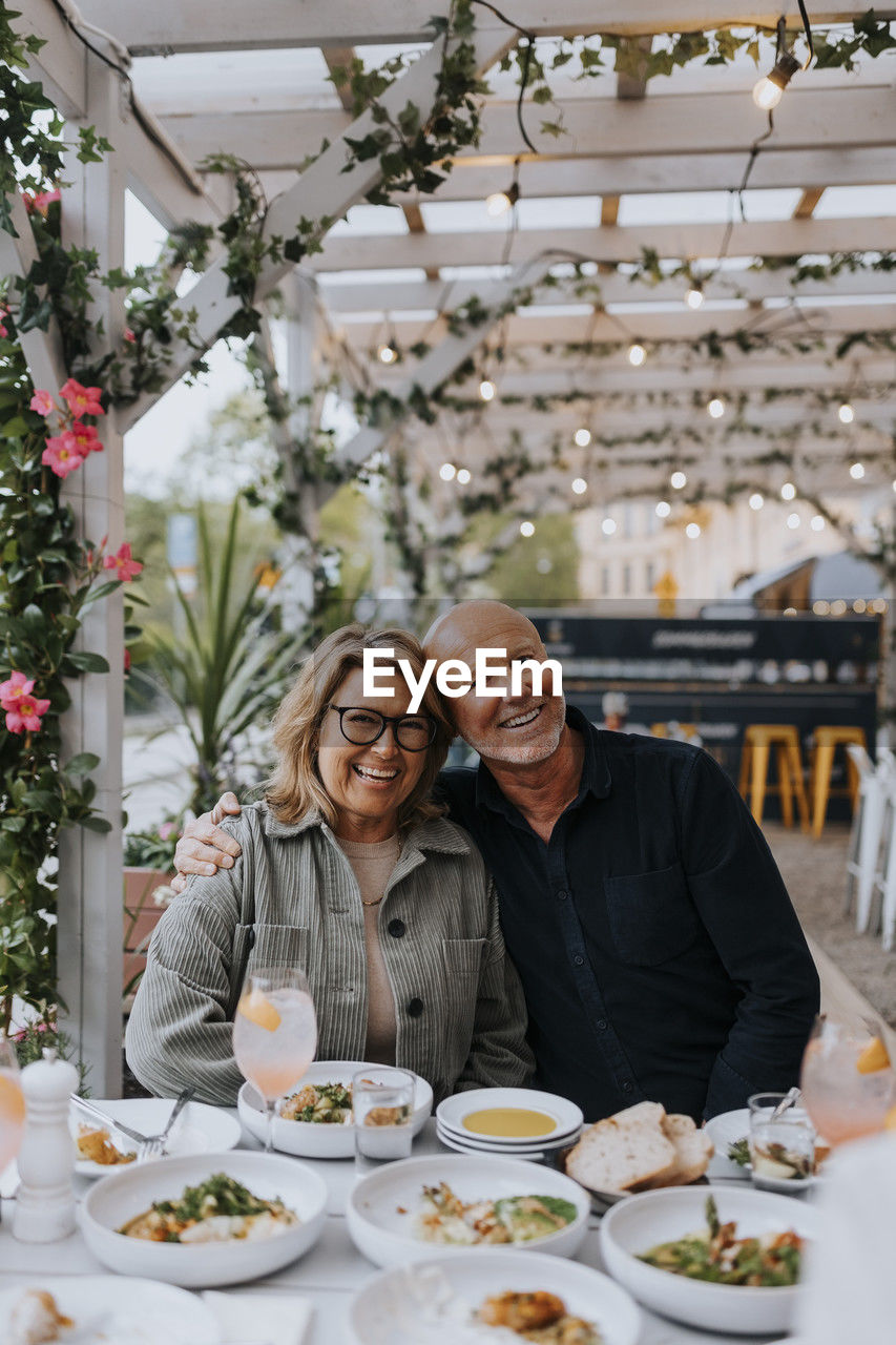 Happy male and female senior friends sitting with food on table at restaurant