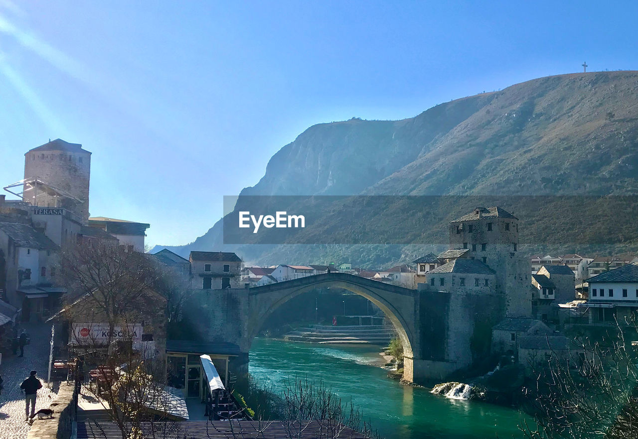 Bridge over river amidst buildings in city against sky