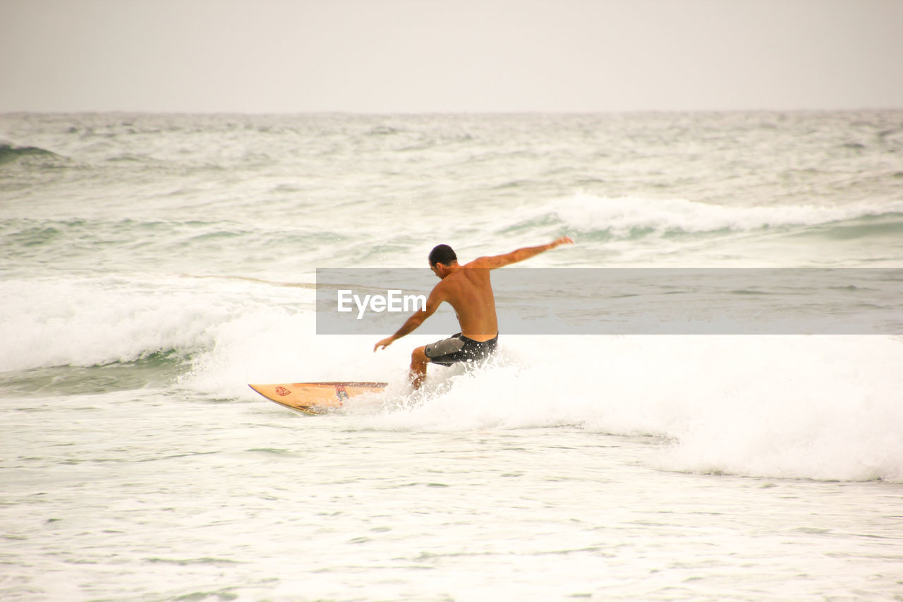 REAR VIEW OF MAN SURFING ON BEACH