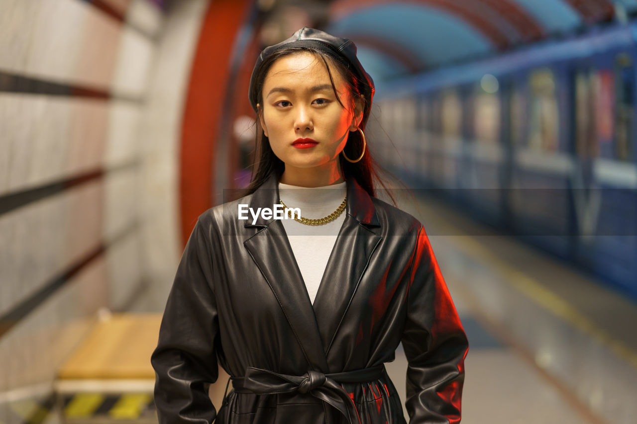 Stylish asian girl in leather beret and trench coat wait for train at underground metro station
