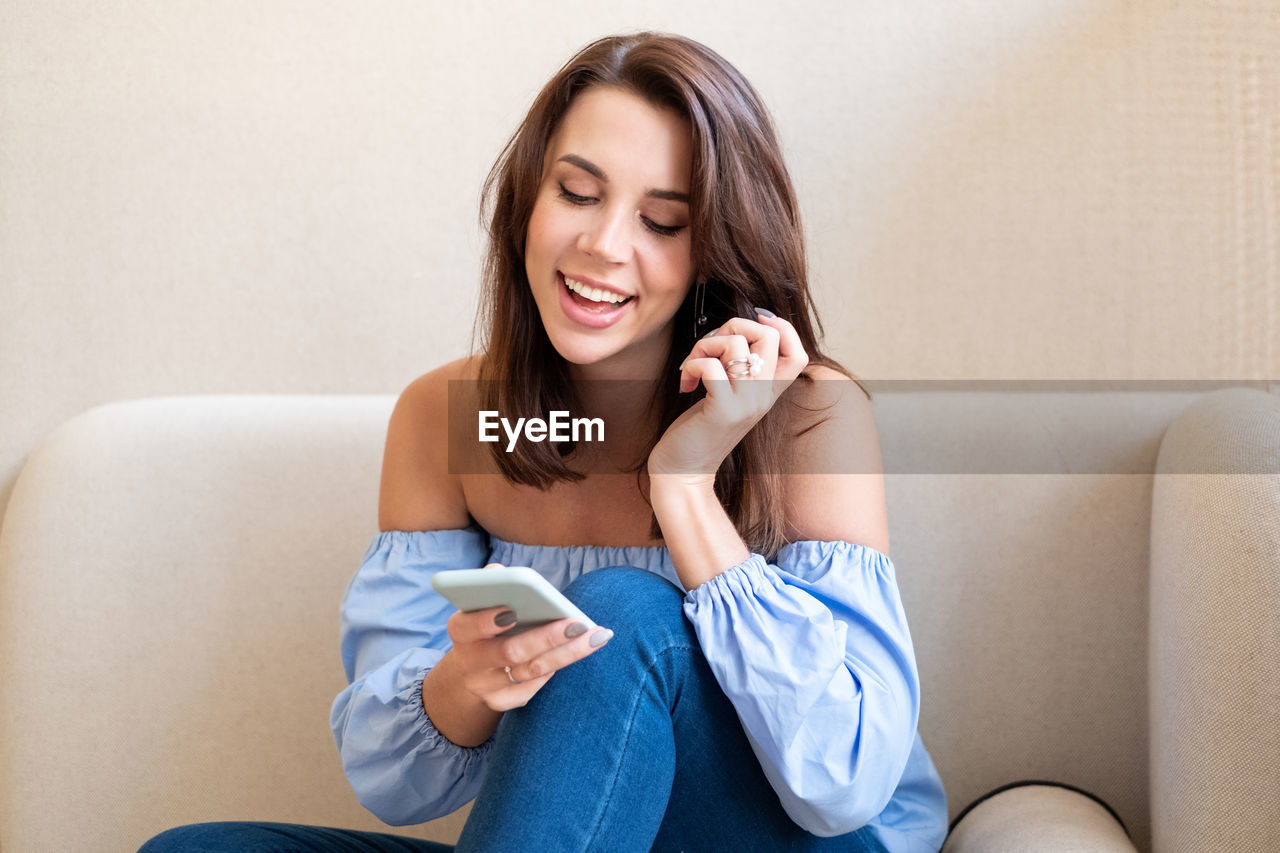 Smiling woman using phone while sitting on sofa