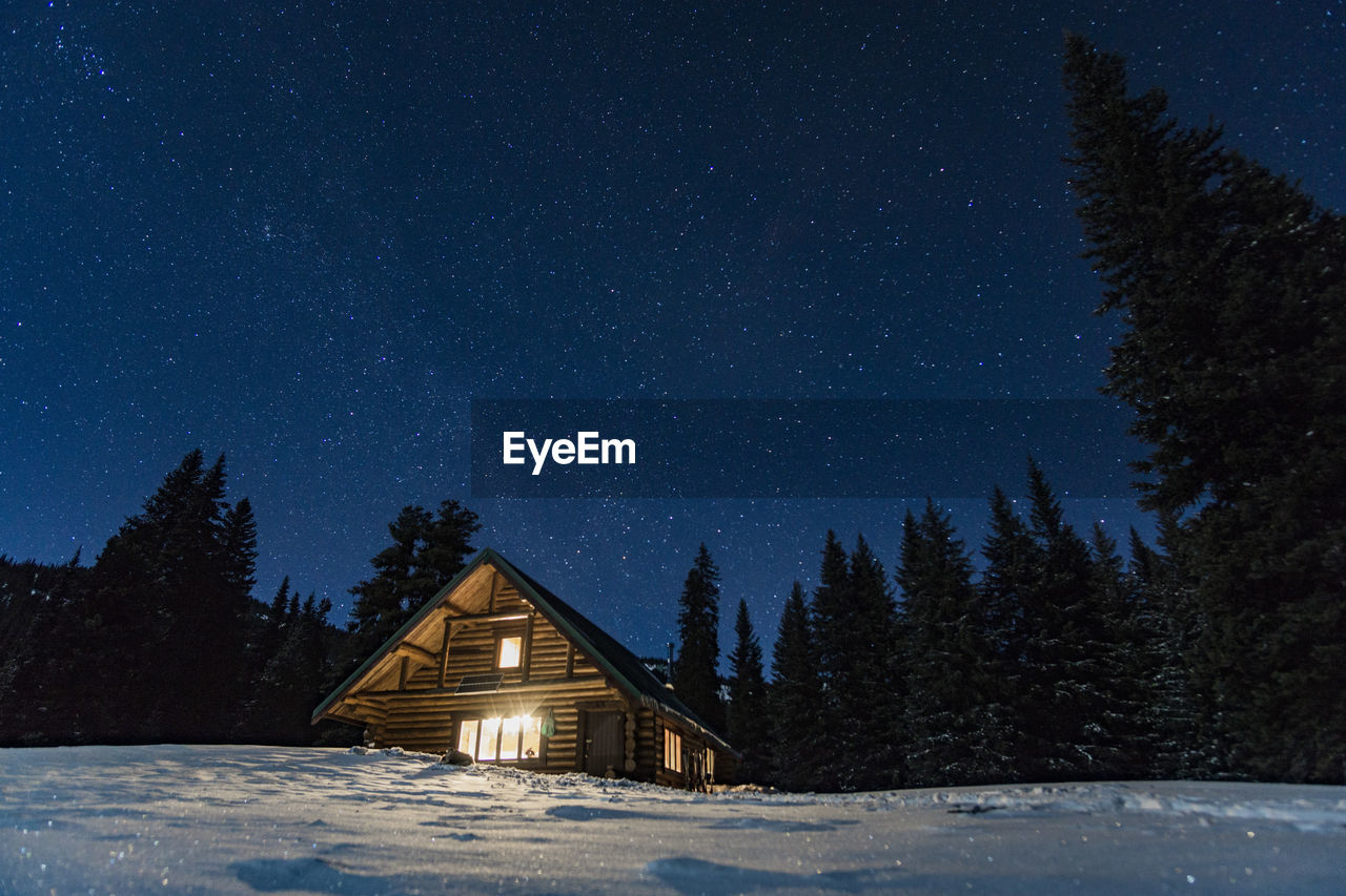 Illuminated house on snowcapped landscape against star field sky