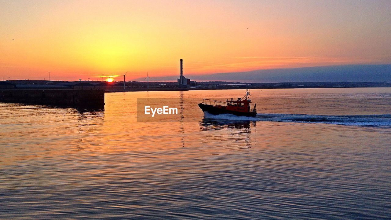 BOAT SAILING ON SEA AGAINST ORANGE SKY