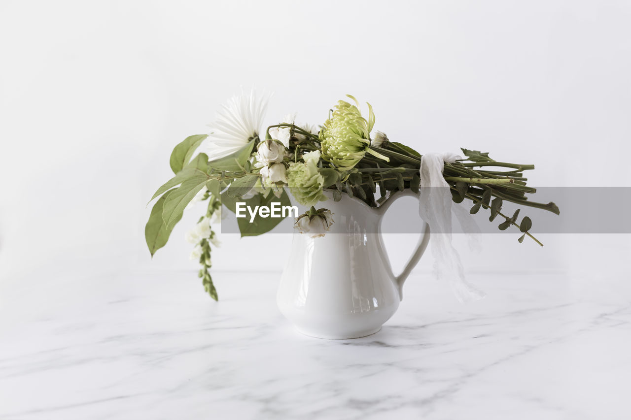 Flower bouquet tied with linen ribbon laying on top of white pitcher