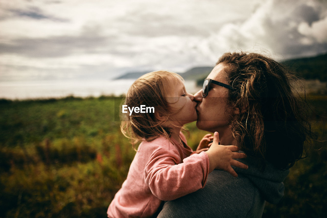 Side view of mother kissing daughter while standing on land