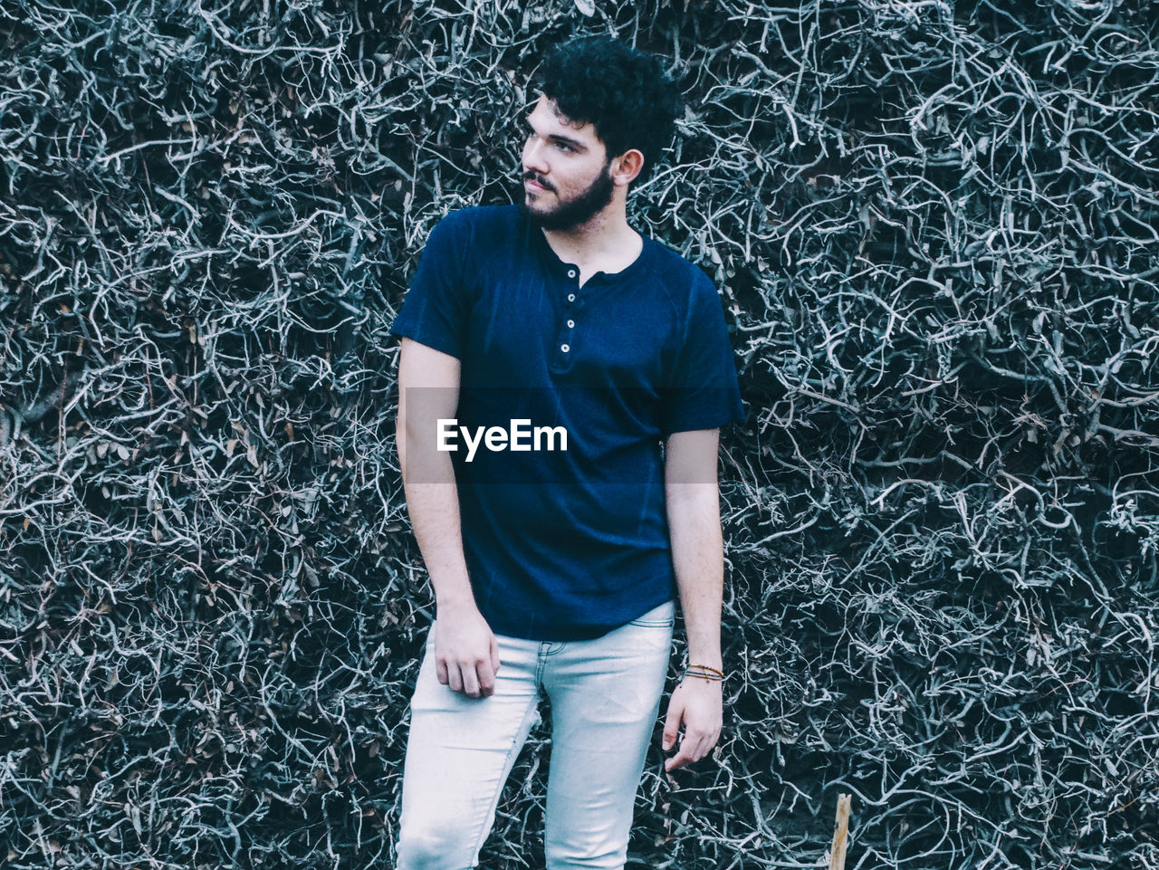 Handsome young man looking away while standing against plants