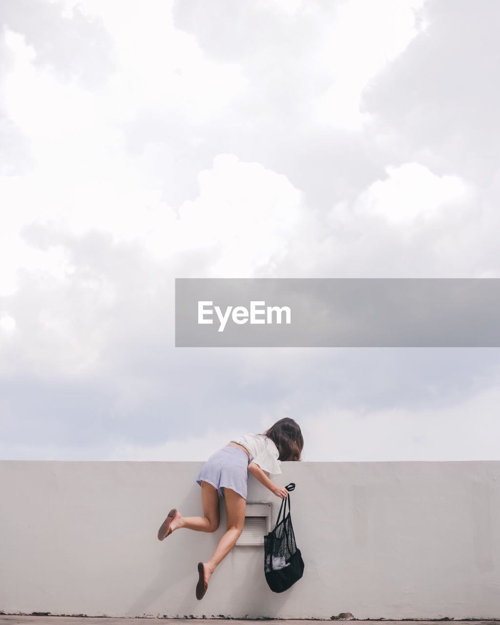 Woman climbing on wall against sky