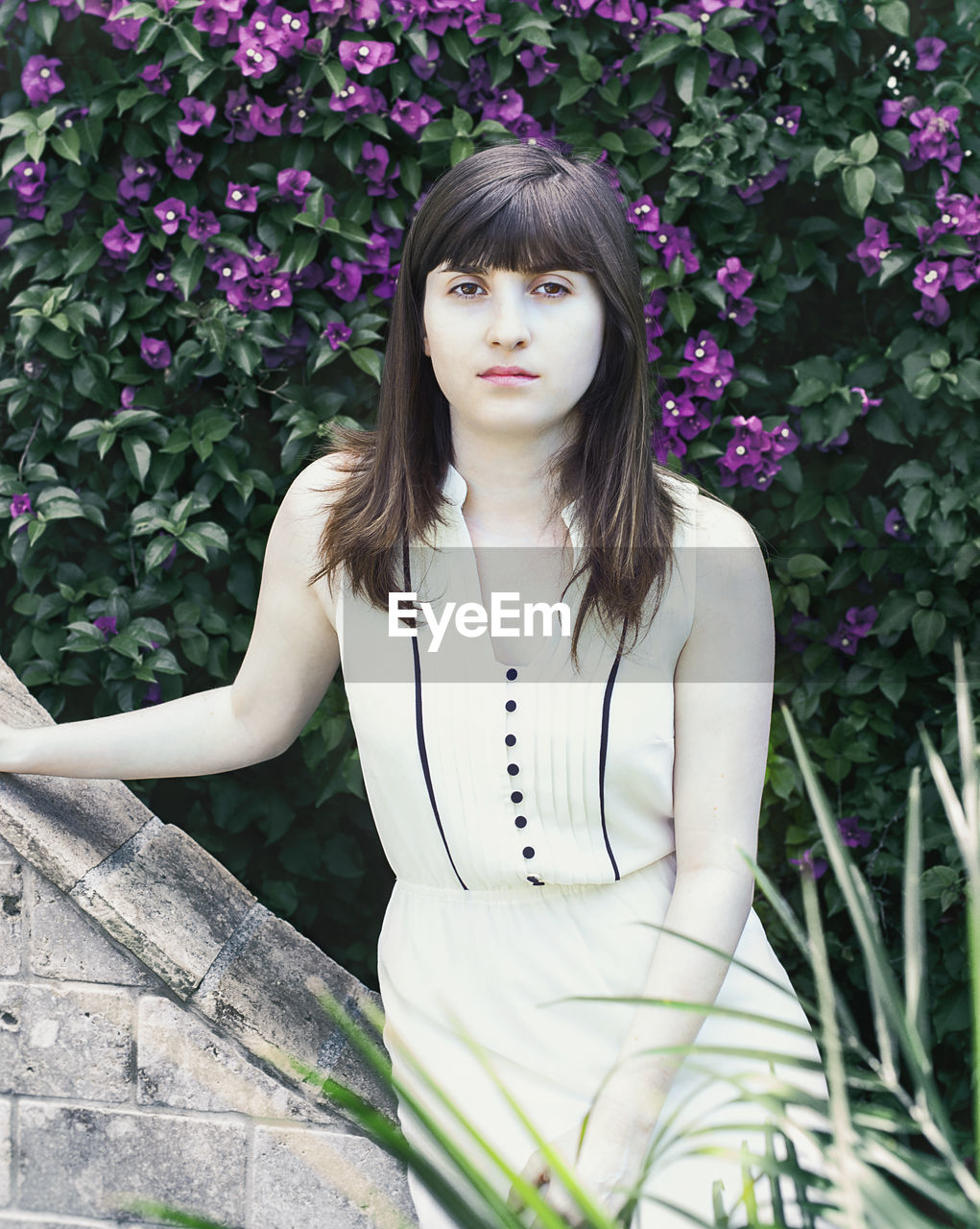 Portrait of serious woman leaning on stone wall against plants