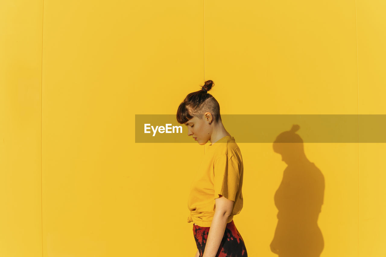 Androgynous person with half-shaved hairstyle standing by yellow wall