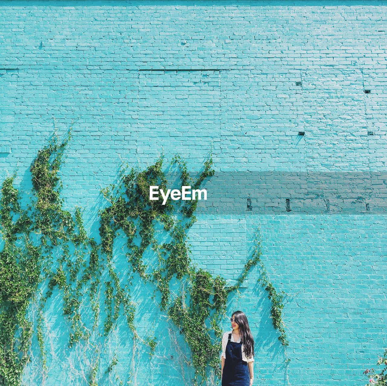 Smiling young woman standing against turquoise wall