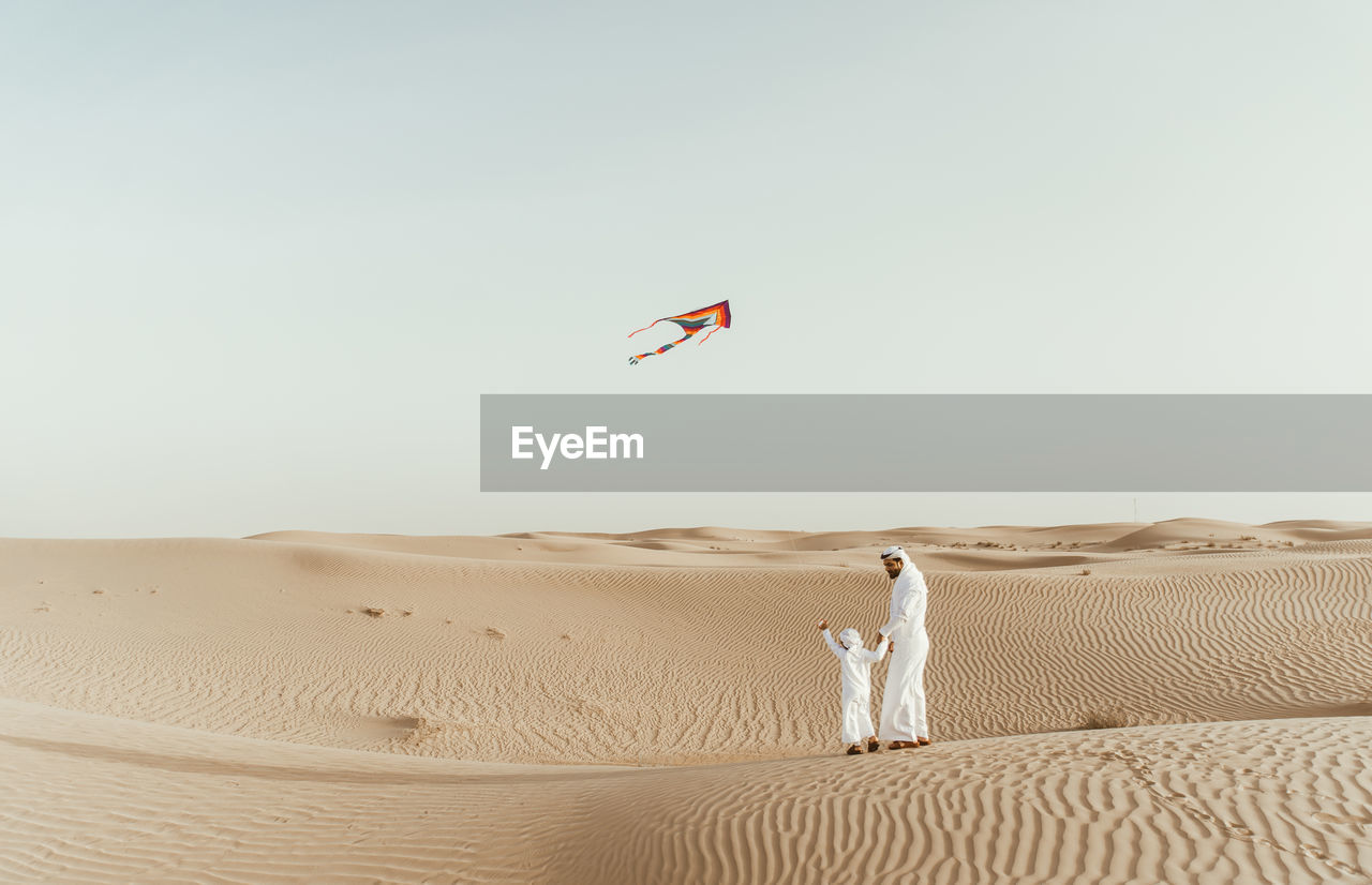 Full length of father with son flying kite in desert