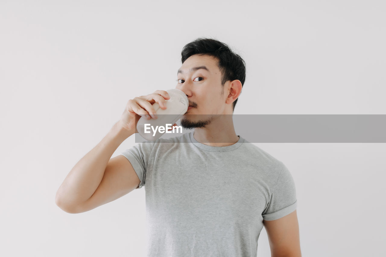 portrait of smiling young woman drinking milk while standing against white background