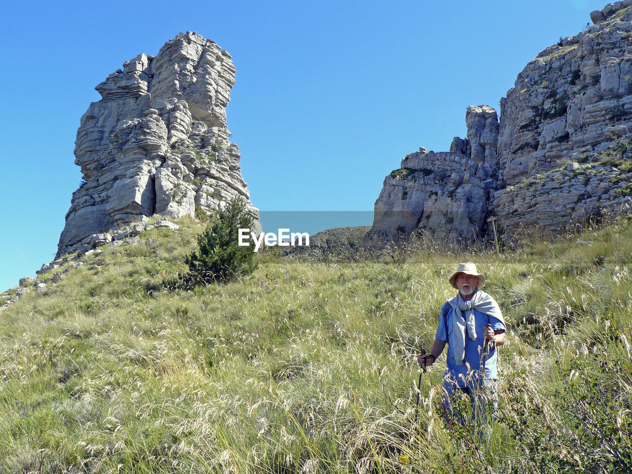 Low angle view of mature man hiking on grassy hill against clear sky