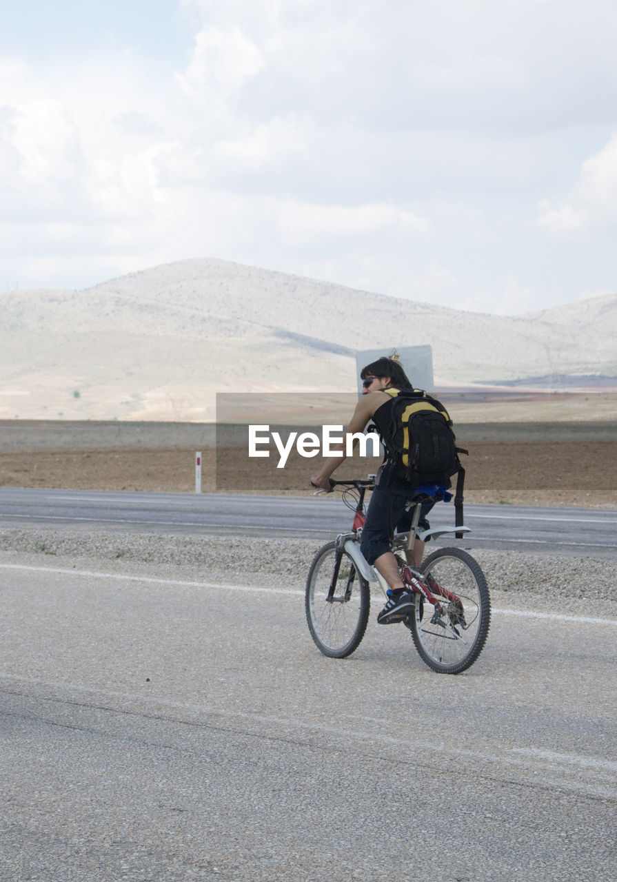 MAN RIDING BICYCLE ON ROAD AGAINST SKY