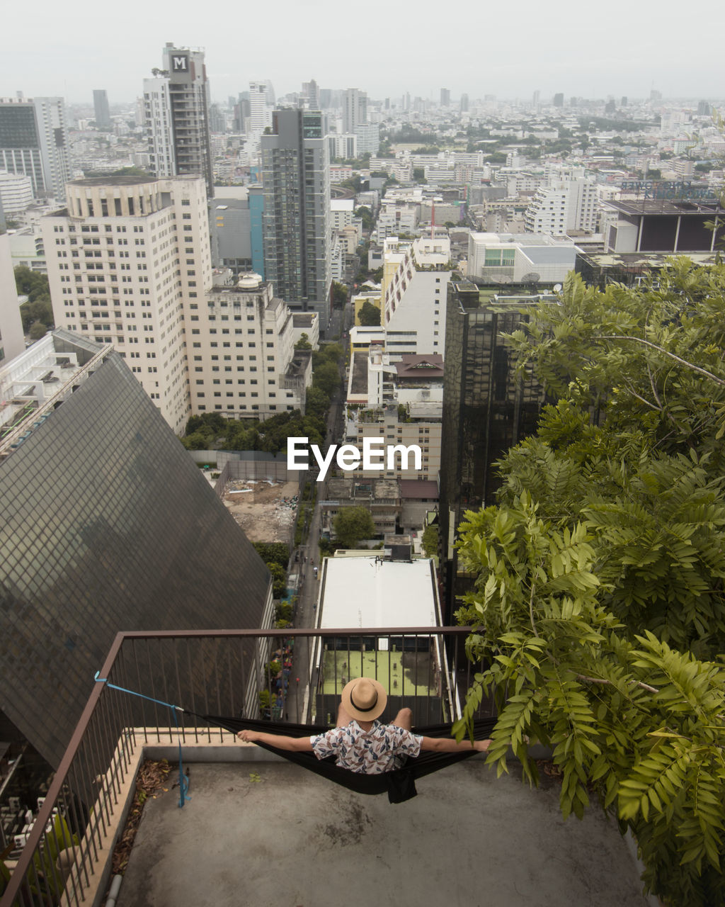High angle view of young man looking at cityscape while sitting on hammock