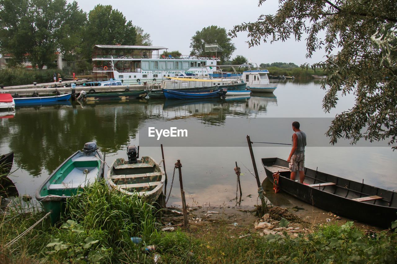 MAN ON BOAT MOORED AT LAKE