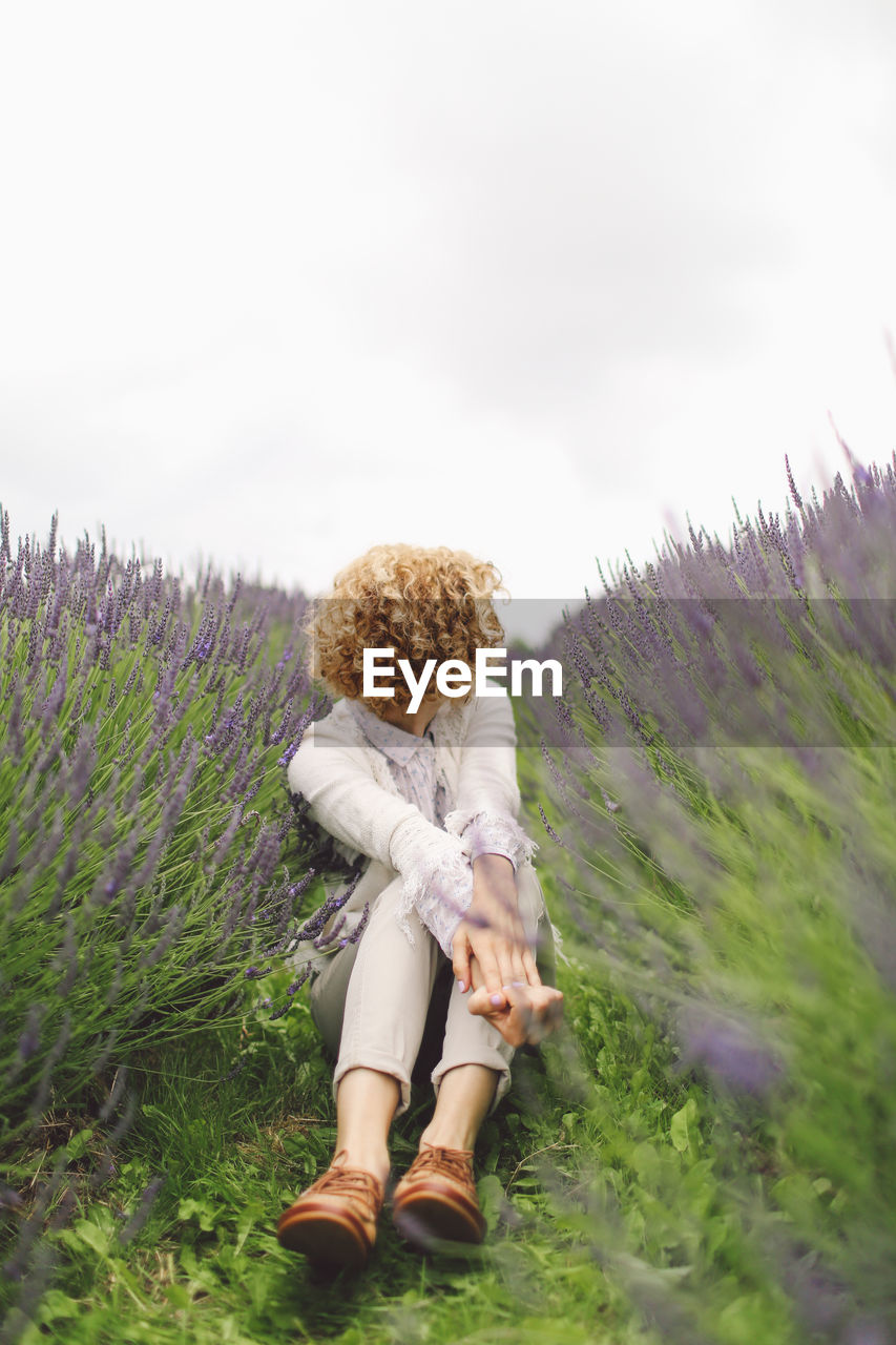 Woman sitting on lavender field against sky