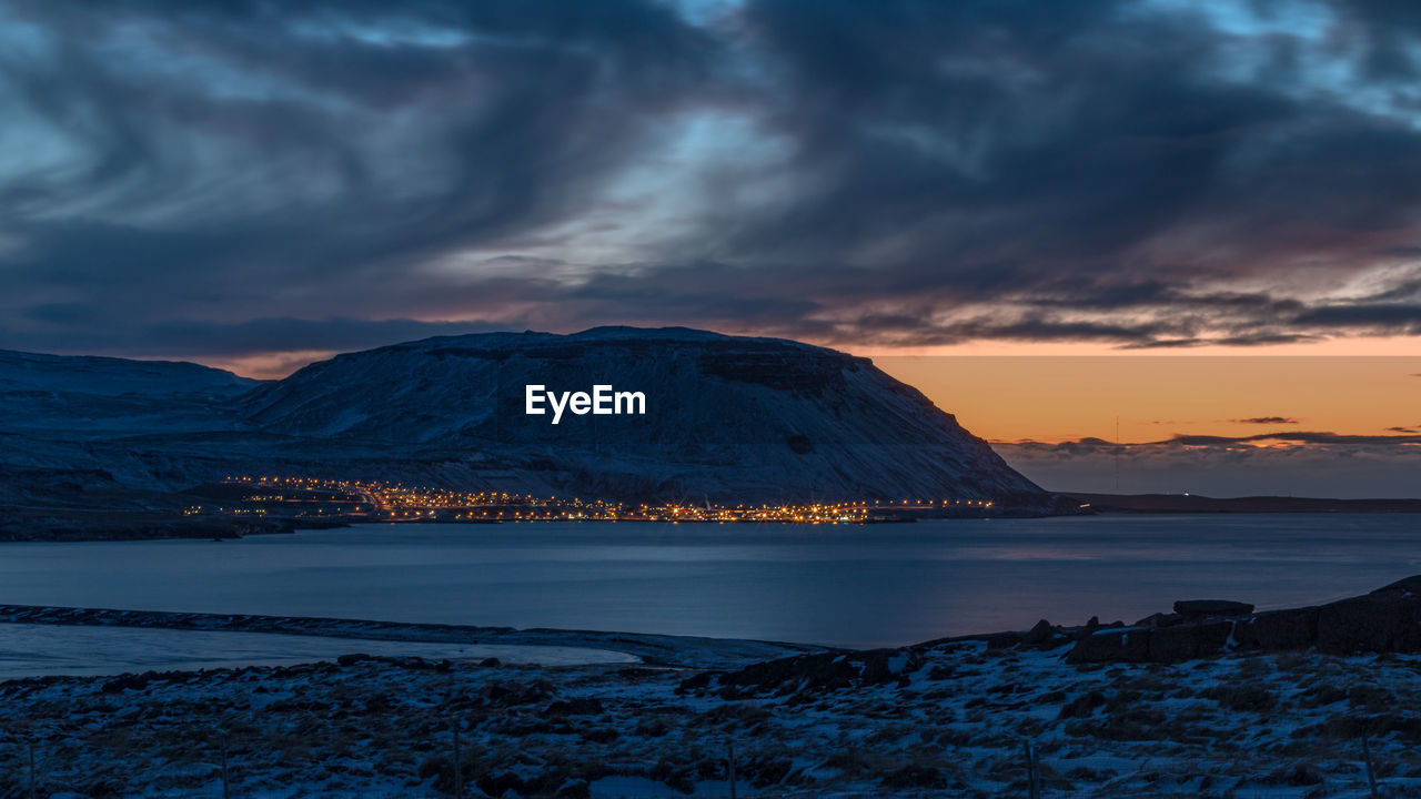 Panoramic view of small city lights at the base of a mountain next to the ocean