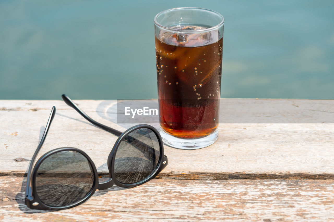 Close-up of cold drink by sunglasses on table outdoors