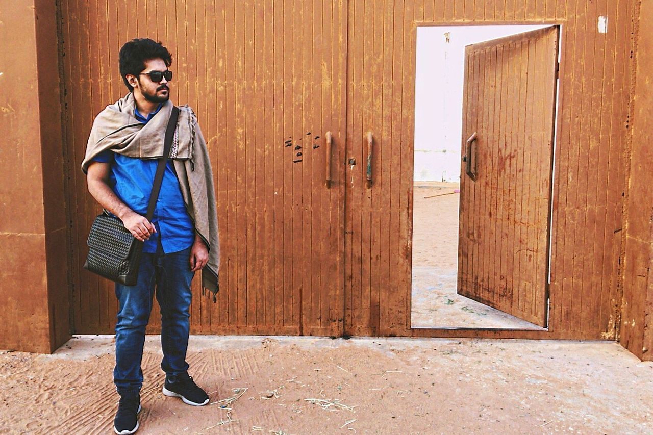 Full length of young man wearing sunglasses while standing by open door