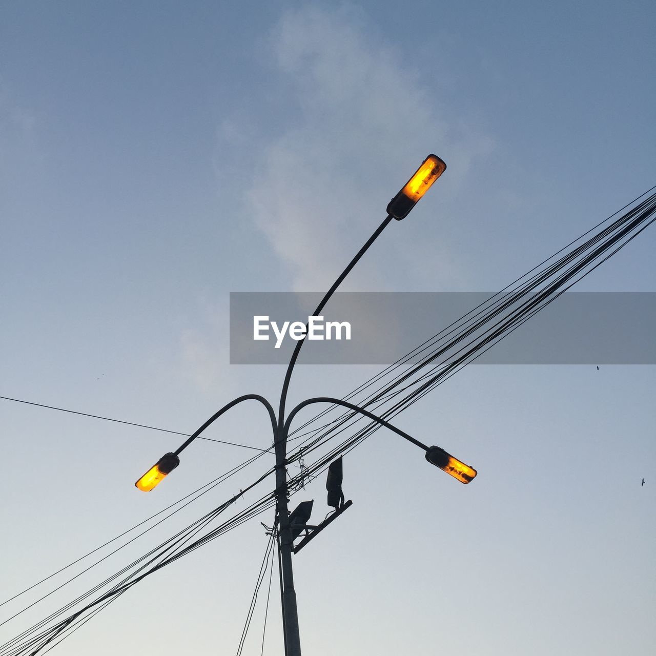 Low angle view of illuminated street light and power lines against sky