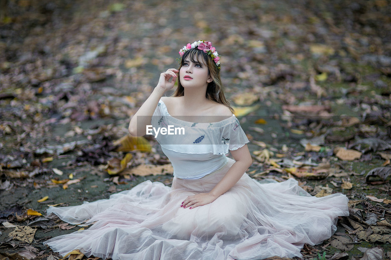 Young woman looking away while sitting on land