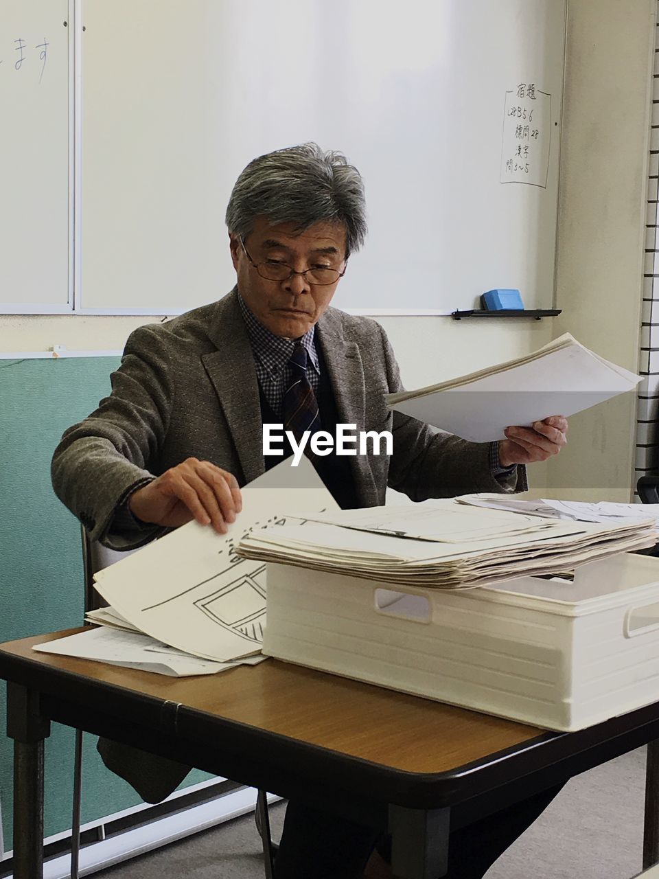 Professor with papers on desk sitting in classroom
