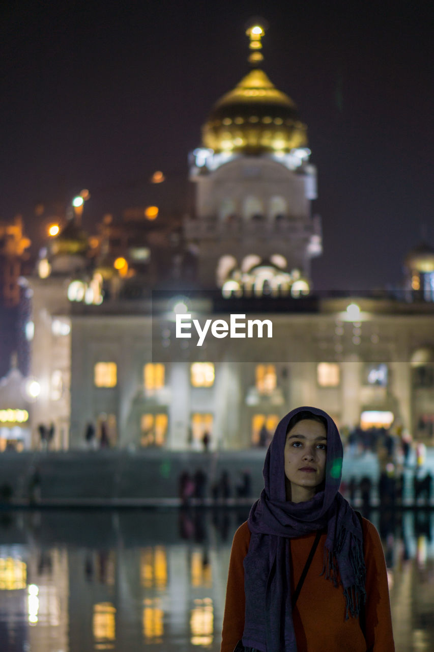 Portrait of woman standing against illuminated temple at night