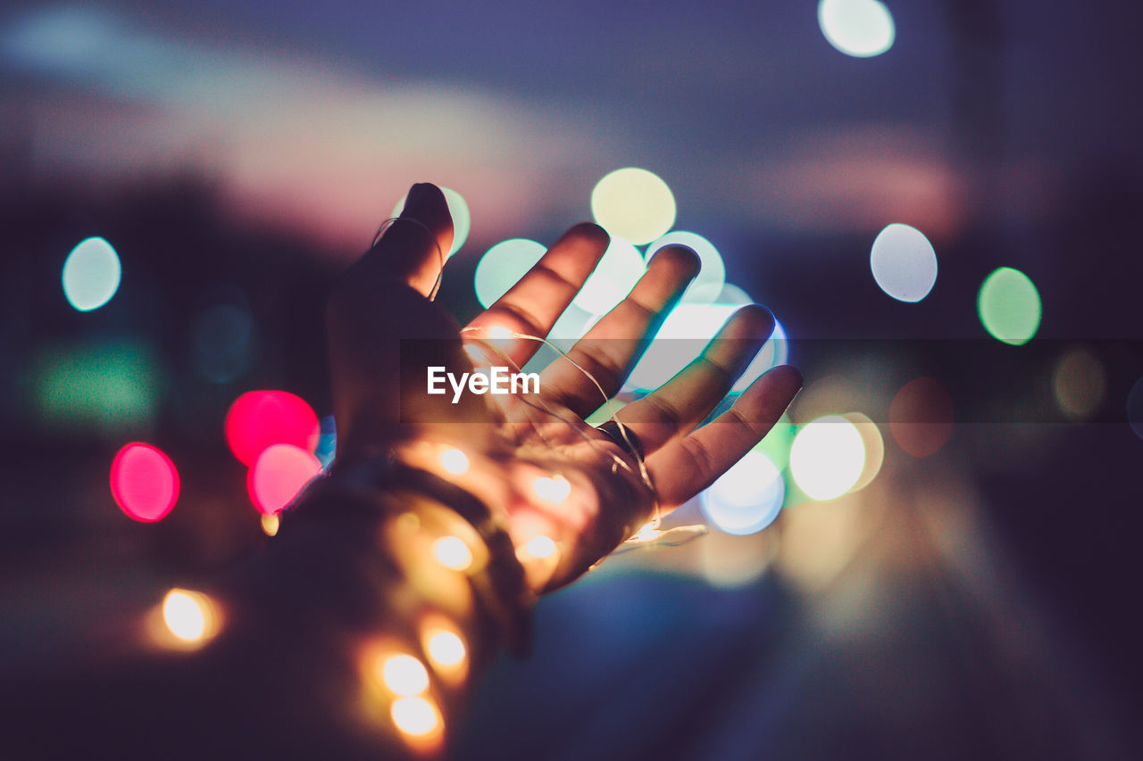 Defocused image of hand holding illuminated lights at night