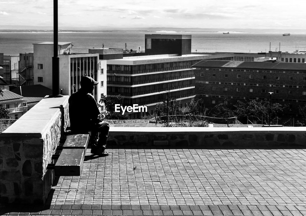 FULL LENGTH OF MAN ON RAILING IN CITY BY SEA