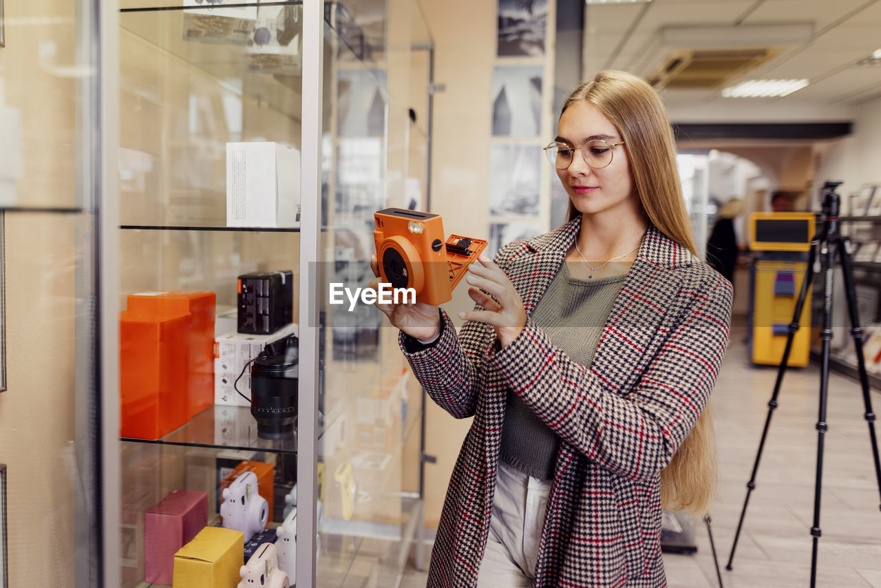 Young woman examining instant camera in shop