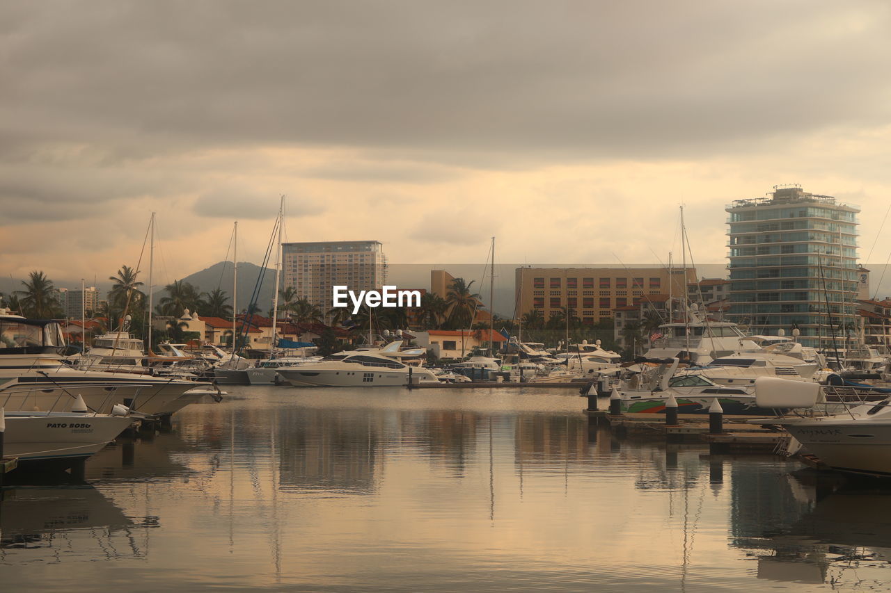 reflection, water, architecture, cityscape, sky, dock, nautical vessel, marina, building exterior, city, built structure, transportation, cloud, harbor, mode of transportation, building, ship, nature, skyline, evening, urban area, moored, no people, vehicle, dusk, sea, sunset, travel destinations, sailboat, skyscraper, waterfront, boat, outdoors, yacht, travel, residential district, landscape, office building exterior, port, watercraft, pier