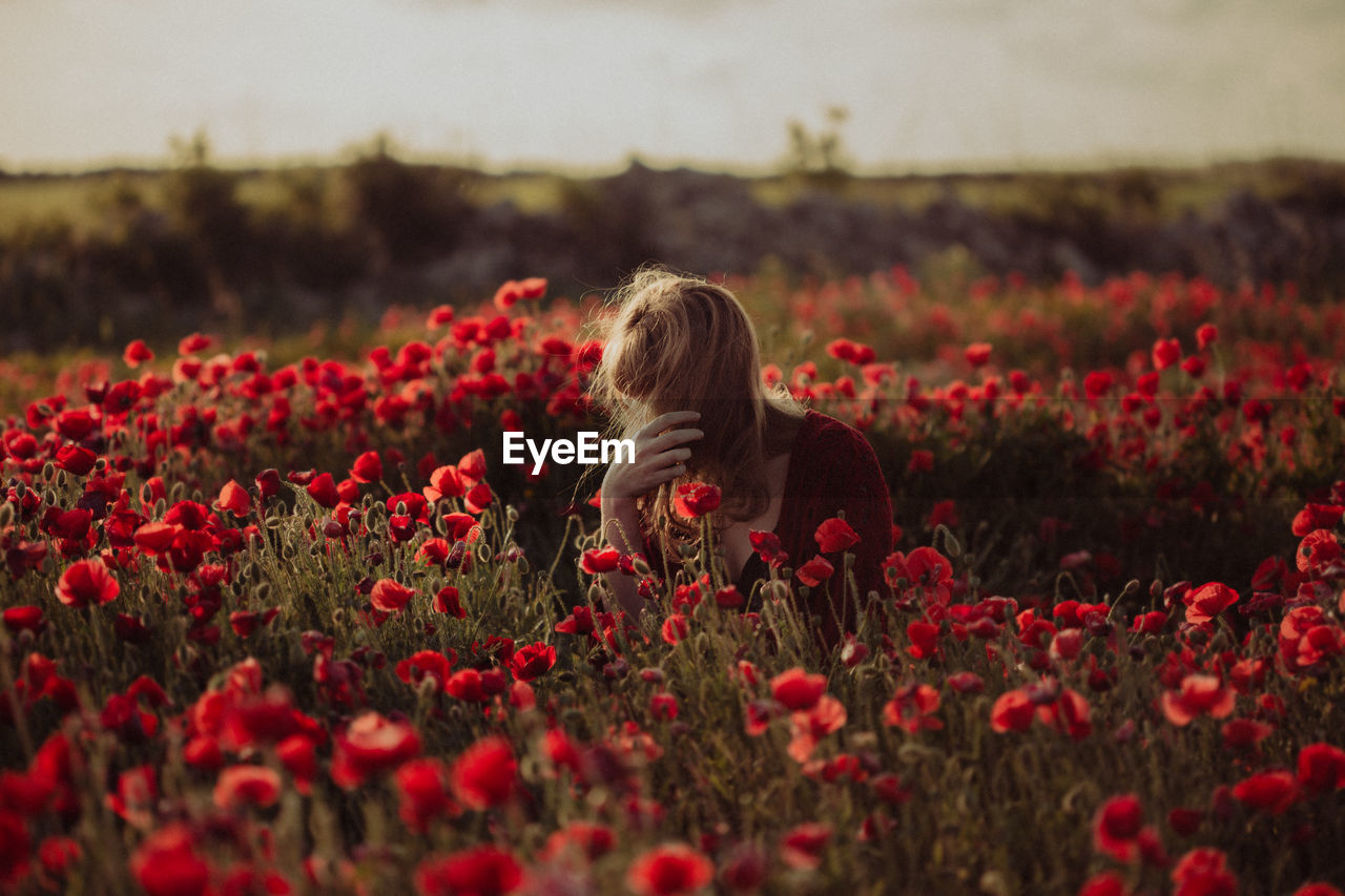 Midsection of woman with red flowers on field