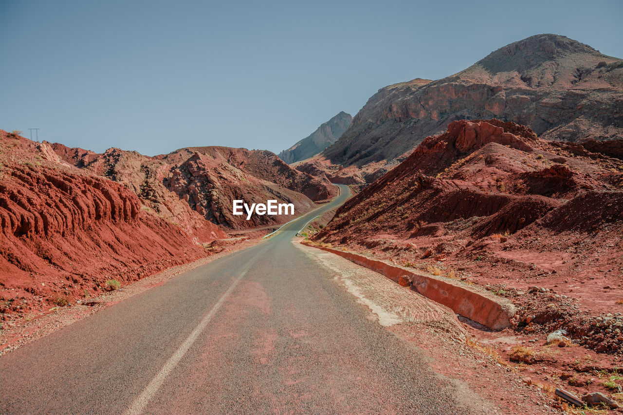 Road leading towards mountains against clear sky