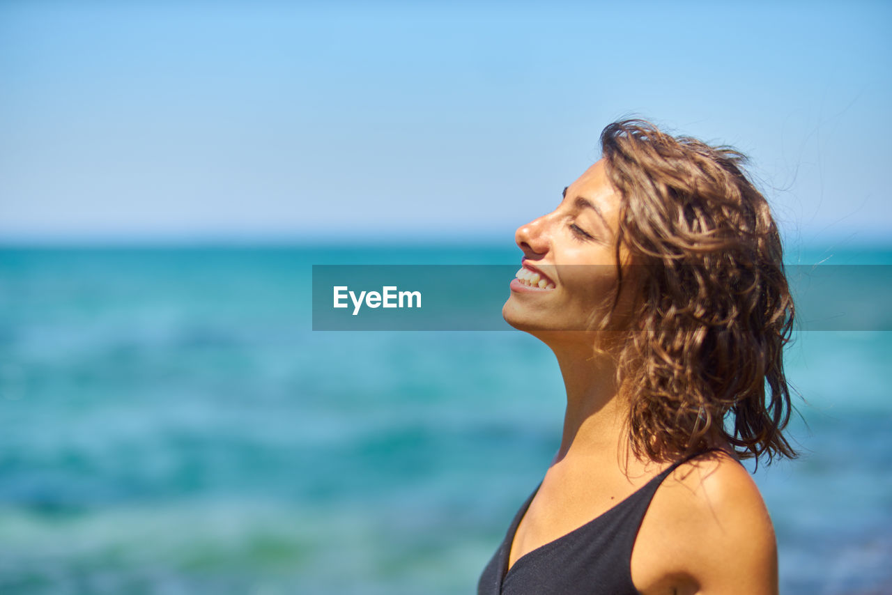 Close-up of smiling young woman against sea