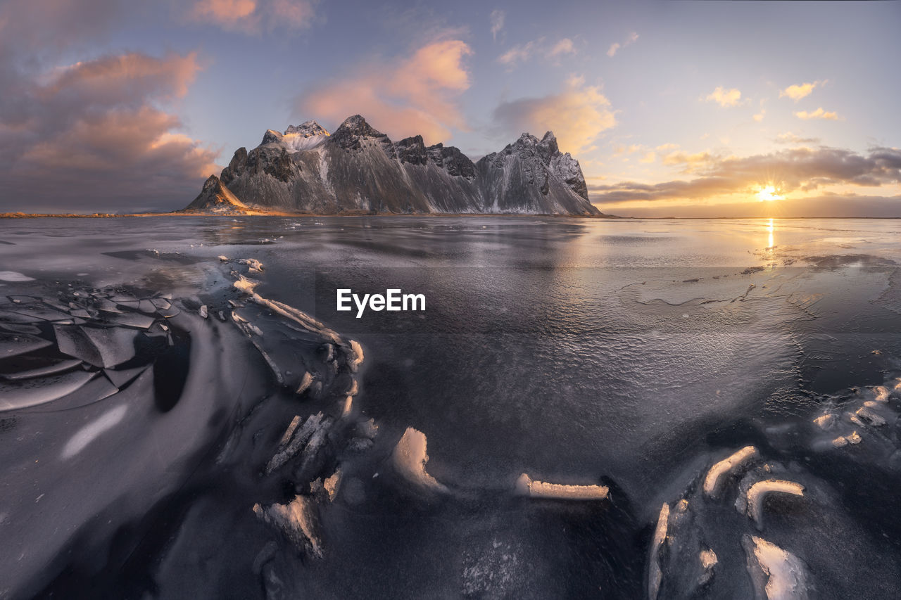 Spectacular view of massive snowy rocky formations surrounded by frozen endless sea during bright sundown